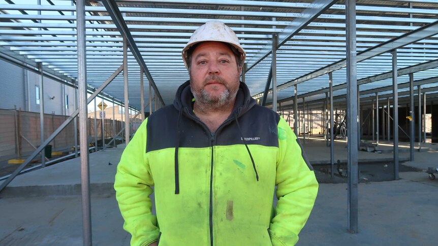 Roofer David Panetta wearing high-vis jacket and hard hat, standing in the metal framework of an industrial building