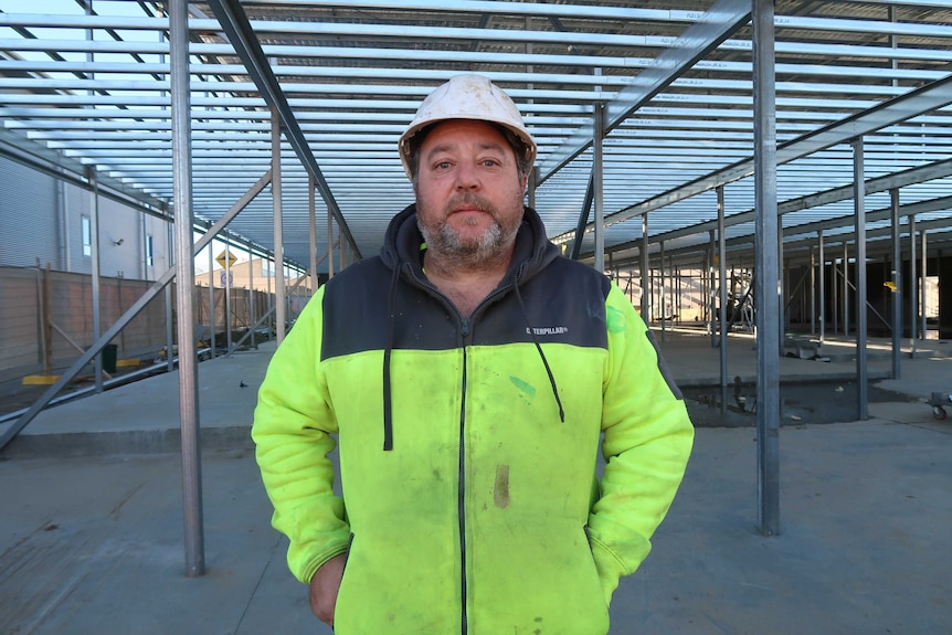 Roofer David Panetta wearing high-vis jacket and hard hat, standing in the metal framework of an industrial building