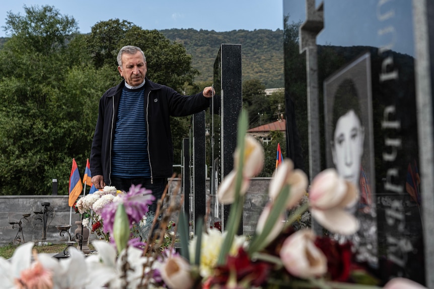 A man wearing dark clothing looks over a row of graves lined with flowers.