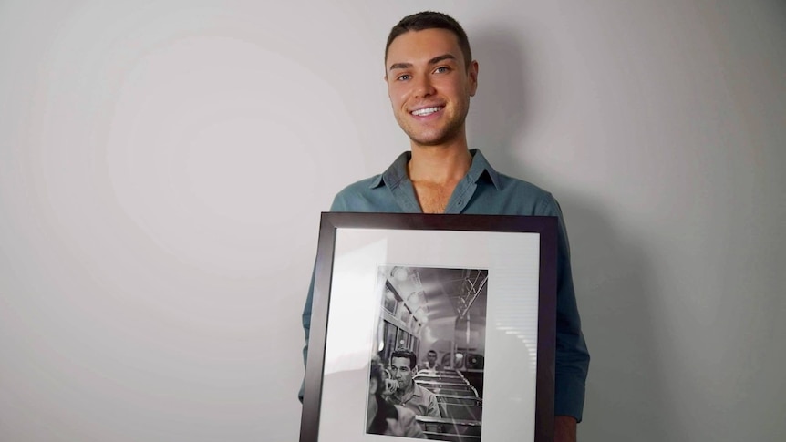 A man smiles as he holds a framed black and white photograph