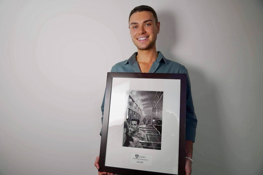 A man smiles as he holds a framed black and white photograph