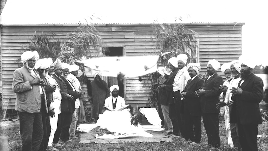 Siva Singh stands under an awning, surrounded by Sikh men.