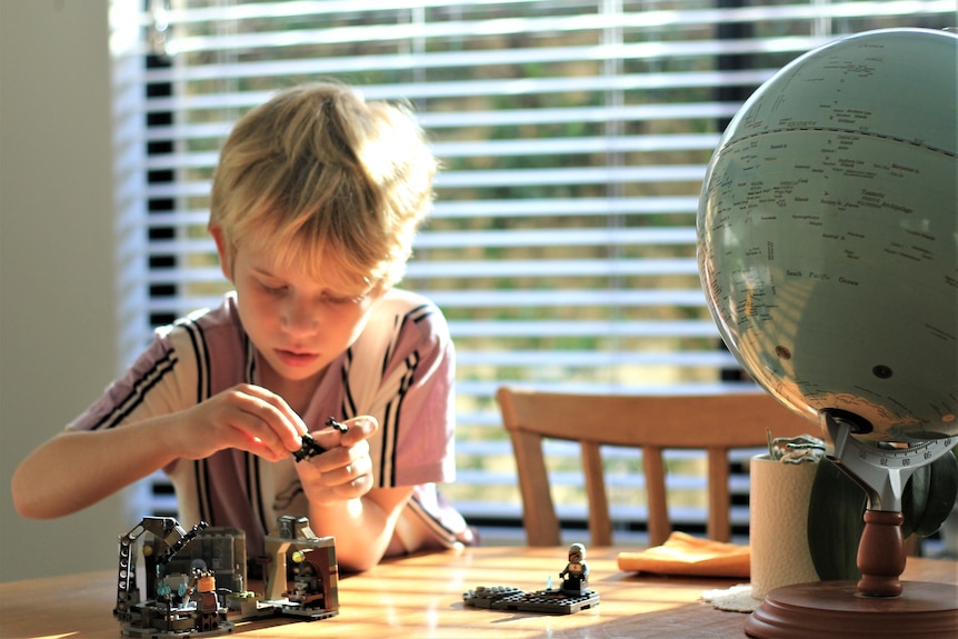 A blond boy with a school globe, building lego