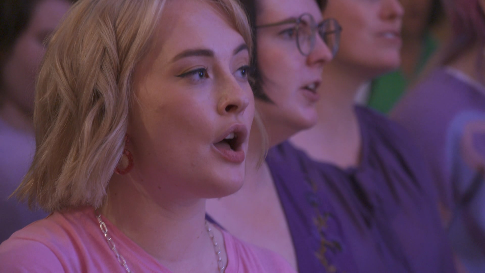 a woman with blonde hair singing with a group of people.