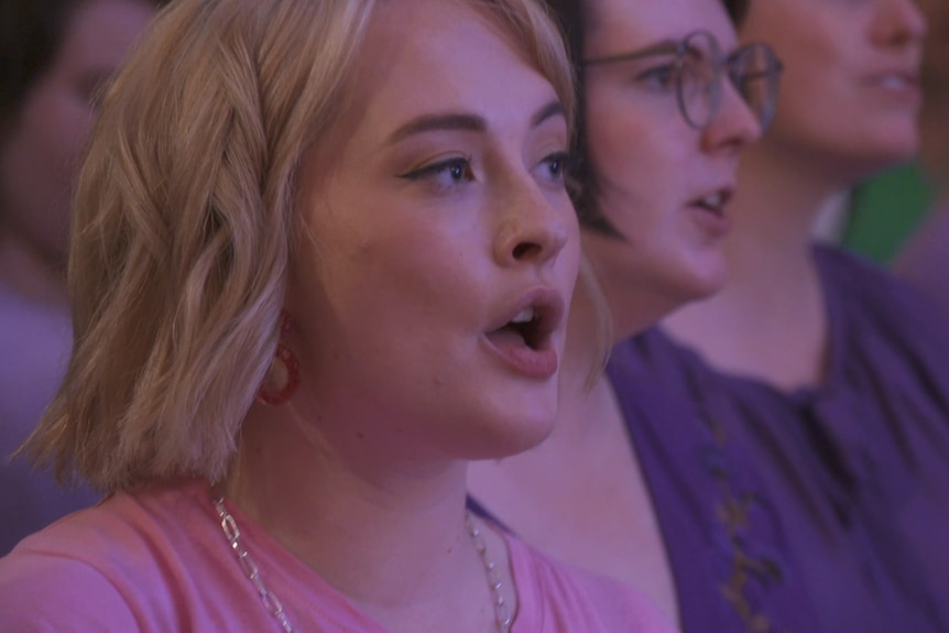 a woman with blonde hair singing with a group of people.