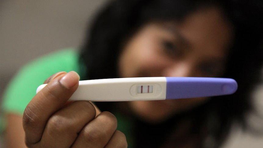 A woman holds up a positive pregnancy test.