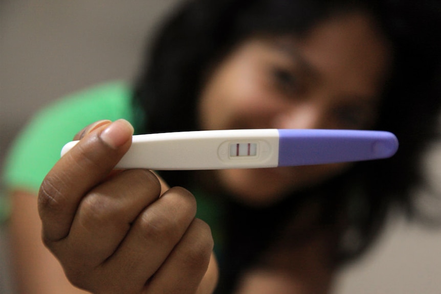 A woman holds up a positive pregnancy test.