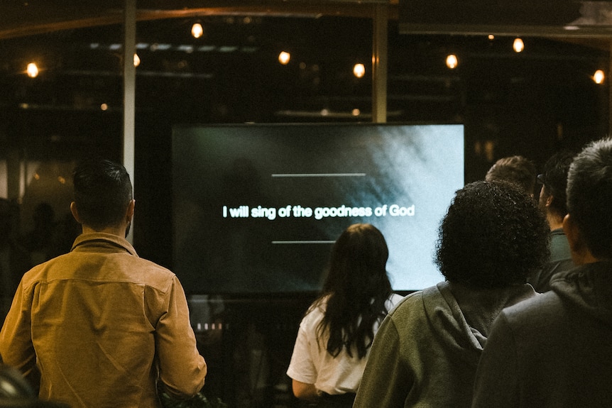 People stand in front of a screen which says: "I will sing of the goodness of God".