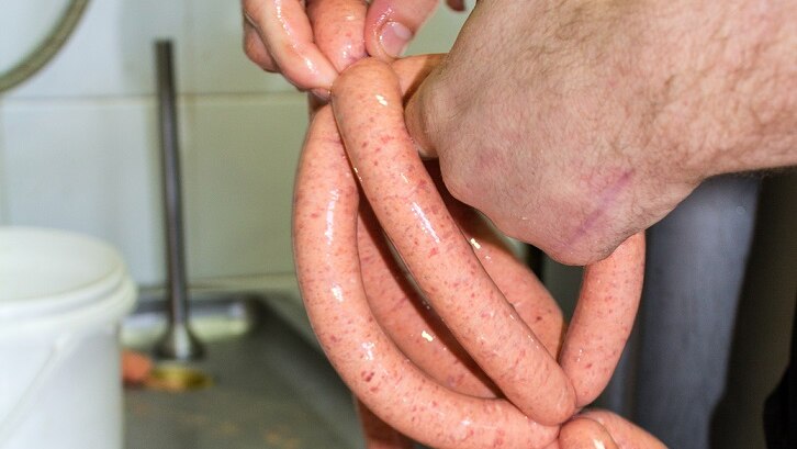 A man's hands hold a string of sausages