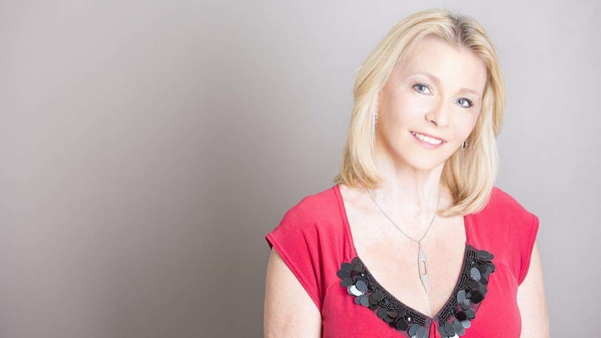 Amanda Lawrie-Jones, with blonde hair and a red top, sits in front of a grey backdrop.