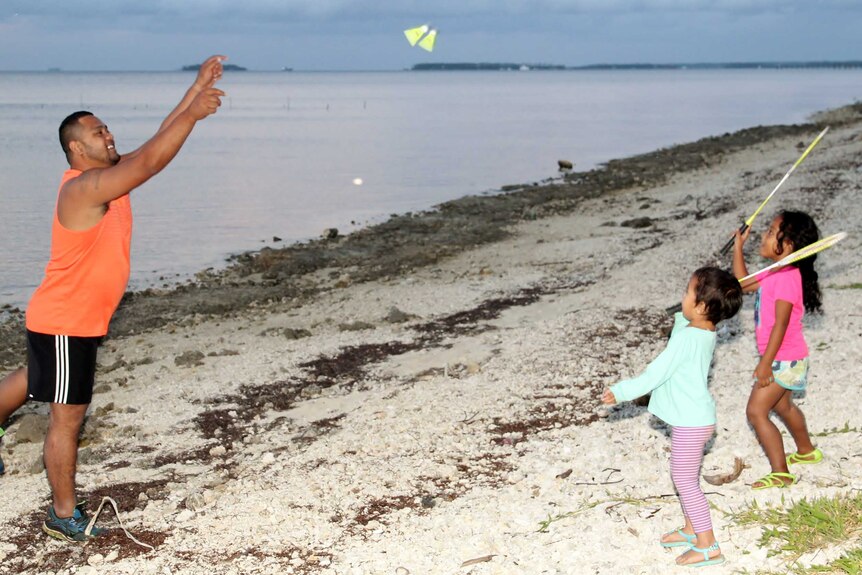 Tevita throw a shuttlecock on the beach and his daughters attempt to hit it