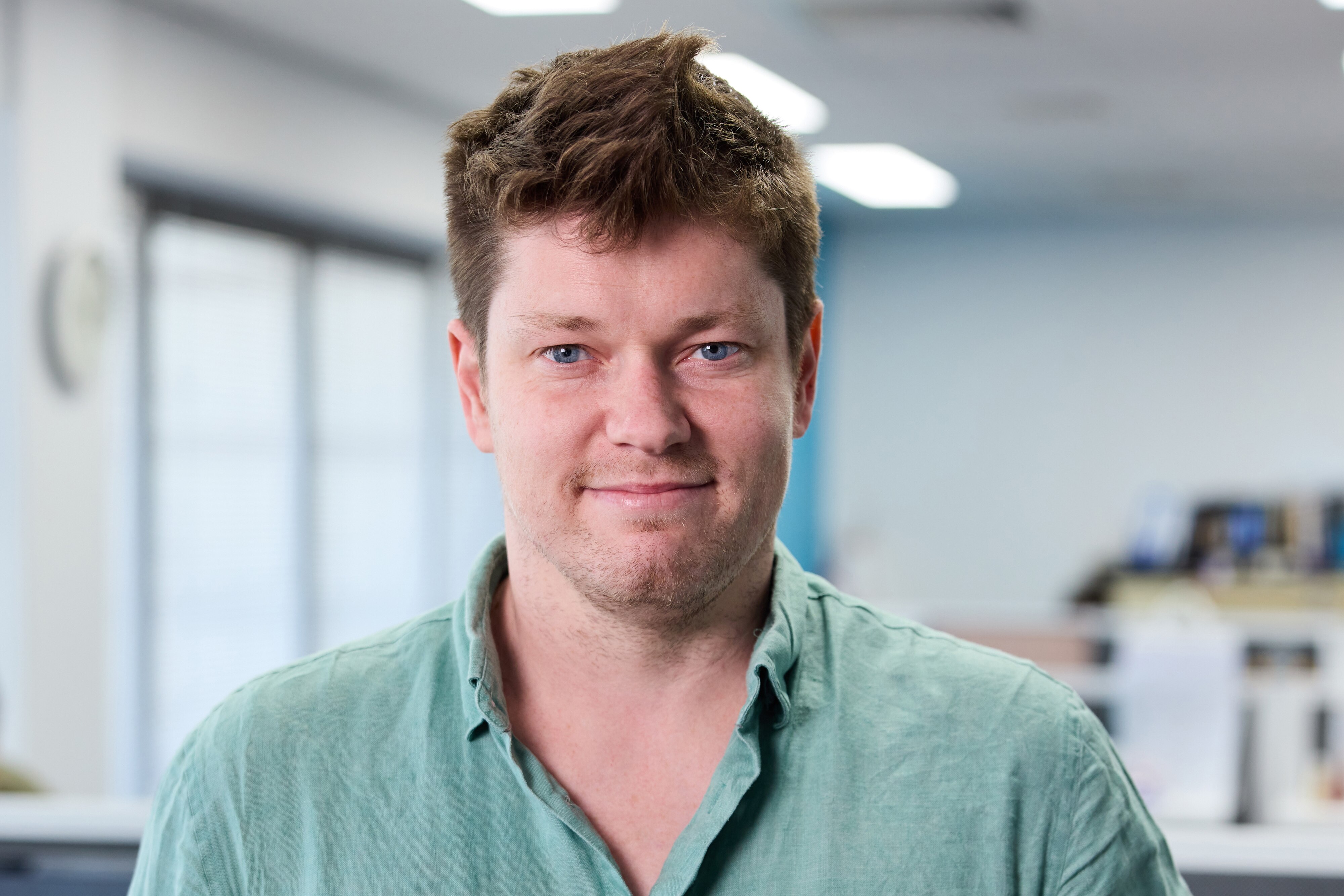 Um homem está em um escritório vestindo uma camisa verde de botões.
