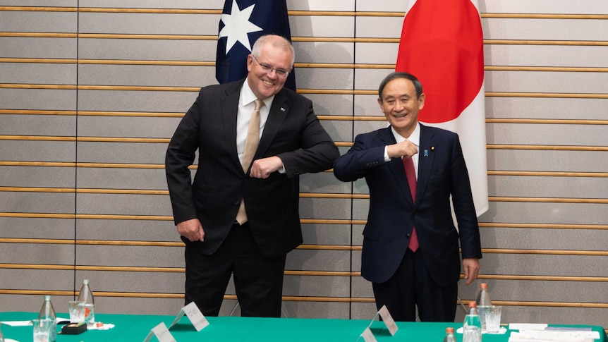 Scott Morrison bumps elbows with Yoshihide Suga. They are smiling.