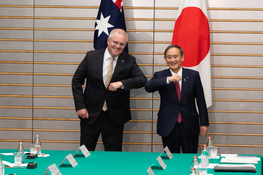 Scott Morrison bumps elbows with Yoshihide Suga. They are smiling.