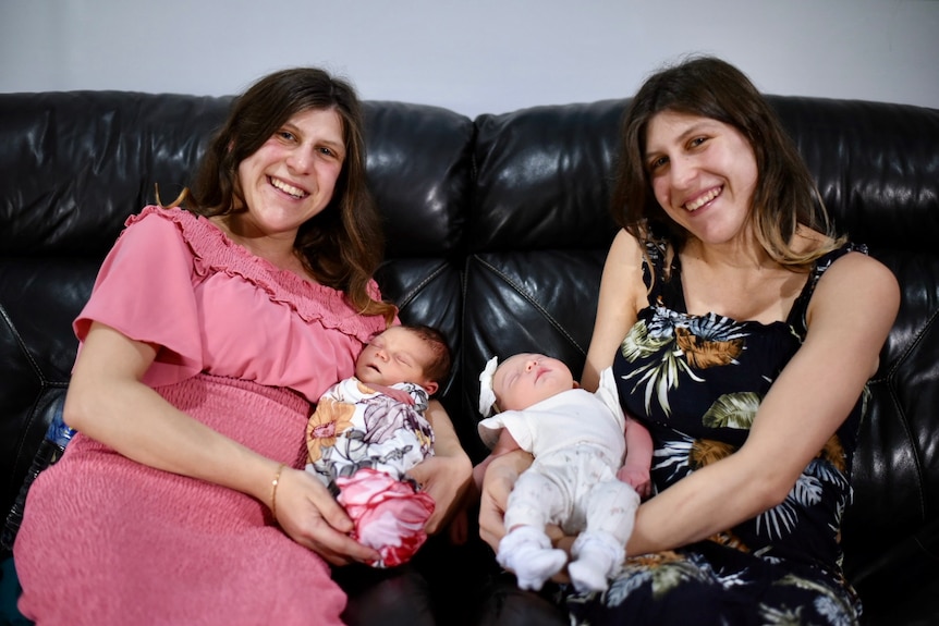 Two mothers hold their babies while sitting on a lounge.