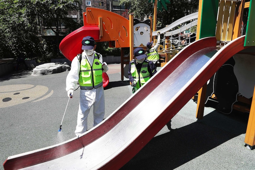 Workers dressed in protective gear disinfect a children's slide.