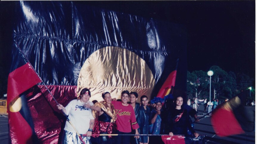 A group of smiling young people march with Aboriginal flags.