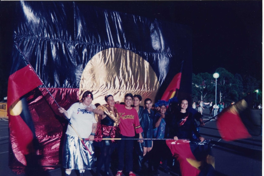 A group of smiling young people march with Aboriginal flags.