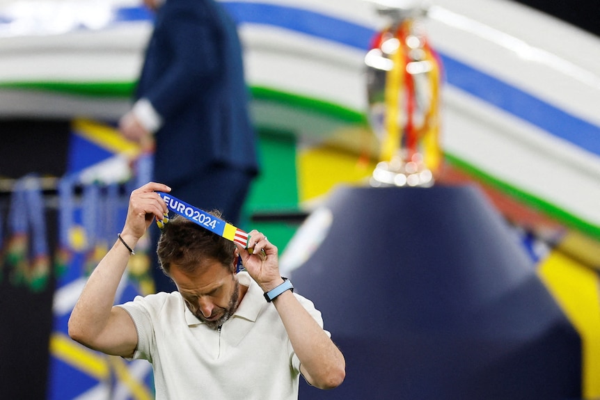 Gareth Southgate removes his runner-up Euro 2024 medal with the winner's trophy in the background
