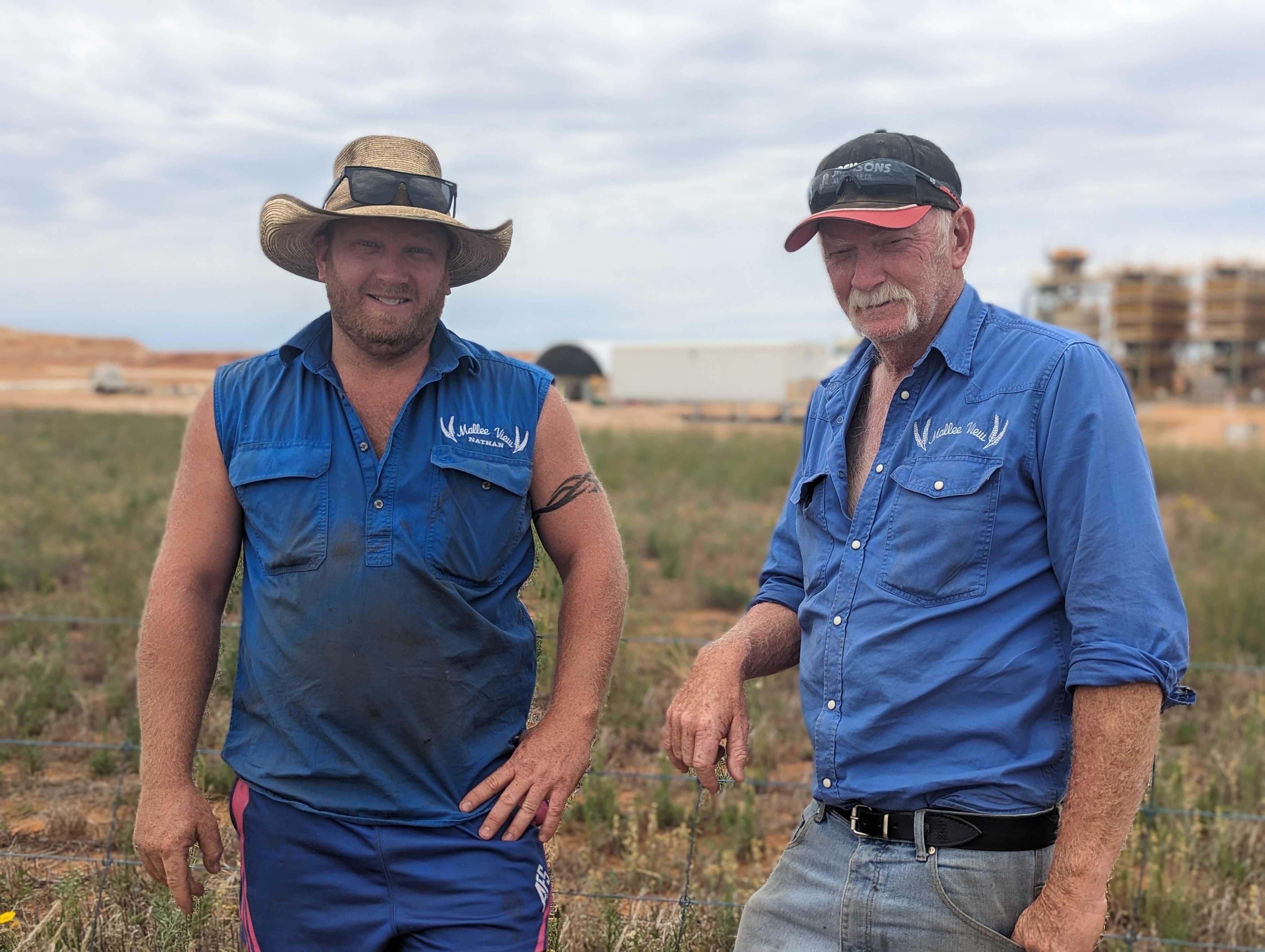 Two fair-skinned male farmers, Kevin and Nathan, in blue work shirts frown on their farm in front of mine site