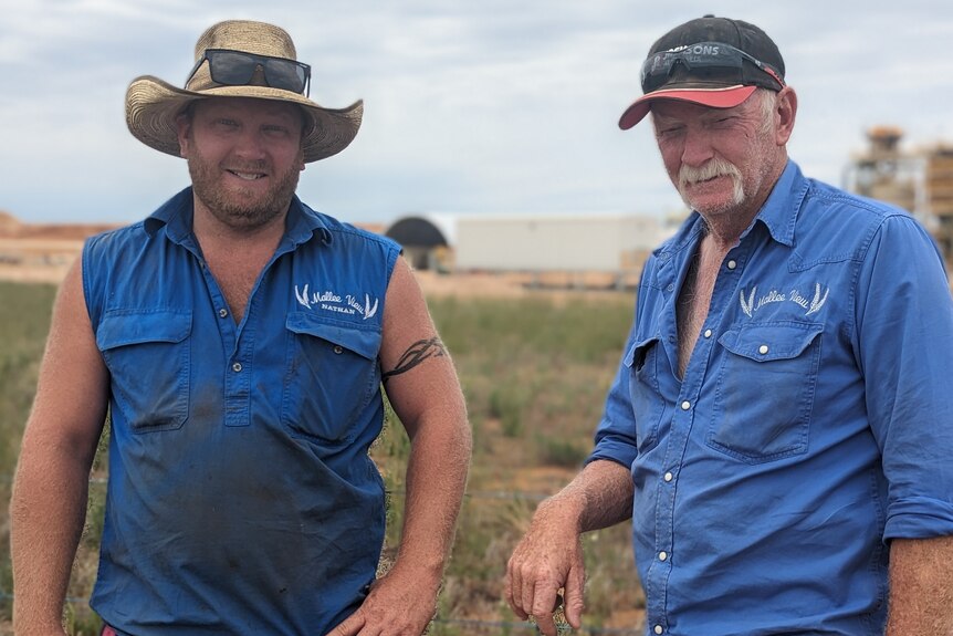 Two fair-skinned male farmers, Kevin and Nathan, in blue work shirts frown on their farm in front of mine site