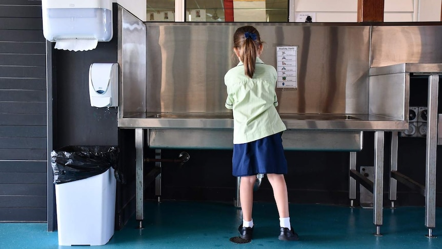 A primary school student washes her hands at a wash trough at Mango Hill State School, north of Brisban.