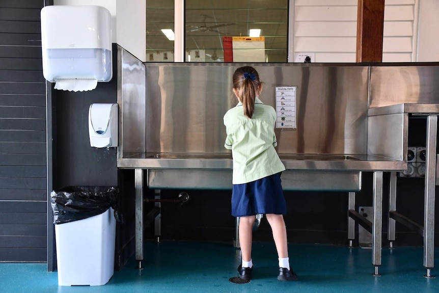 A primary school student washes her hands at a wash trough at Mango Hill State School, north of Brisban.