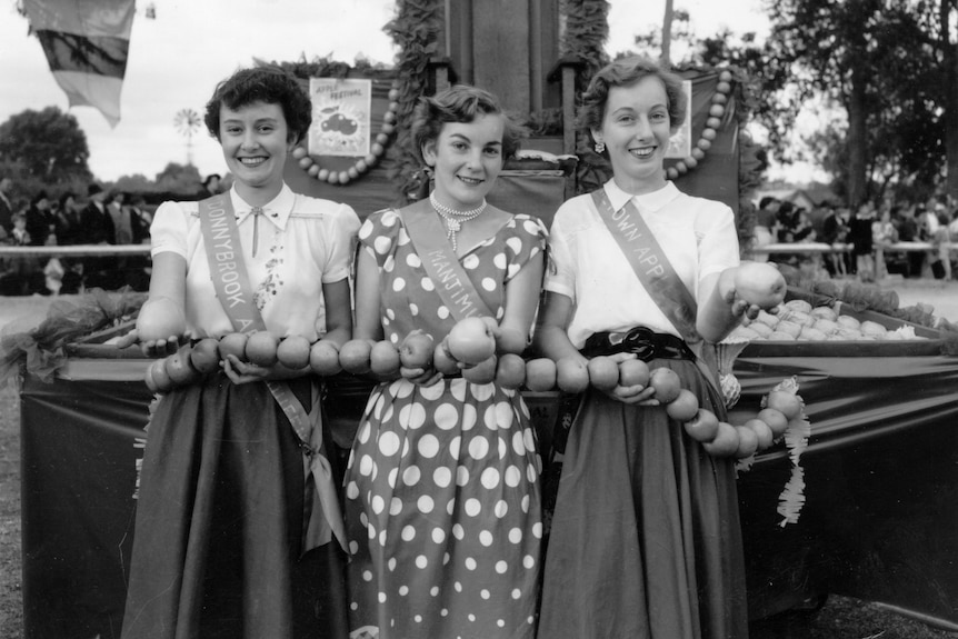 A black and white photo of three women in the 50's holding apples