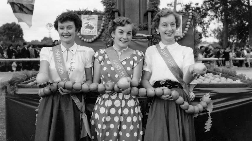 A black and white photo of three women in the 50's holding apples