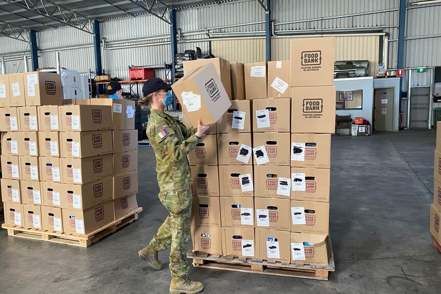 A woman in army fatigues lifting a box in a warehouse