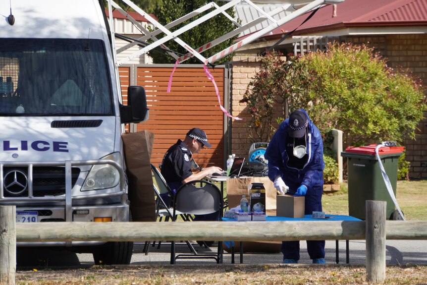 Two police forensic officers work near a police van to process evidence.