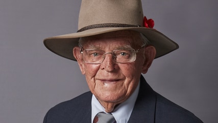An elderly man man dressed in a suit decorated with war medals and an Akruba hat featuring a red poppy.