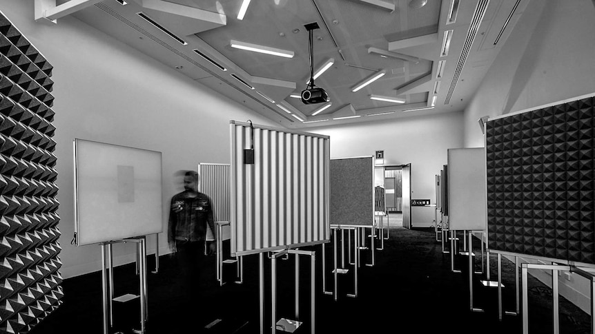 A black and white photo of a room speakers playing sounds into a with many panels mounted on stands.