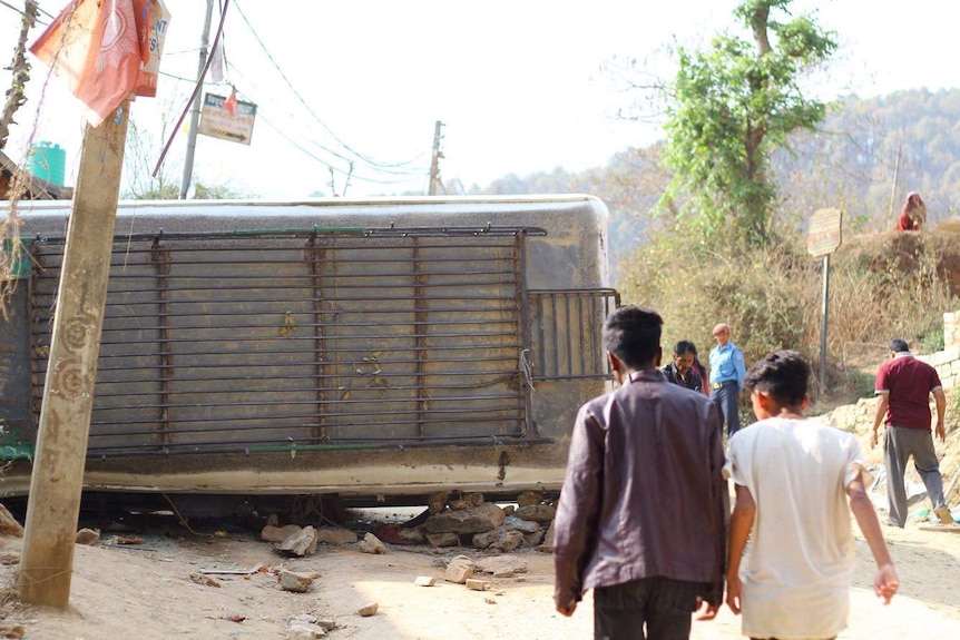 People walk around flipped bus in a town in Nepal.