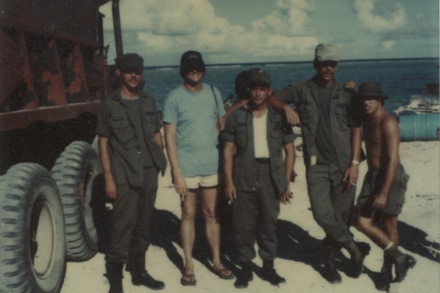 A group of soldiers pose for a photo in front of a truck and the water on Enewetak.