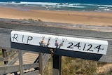 A sign at a beach says "R.I.P" and has the initials of four people.