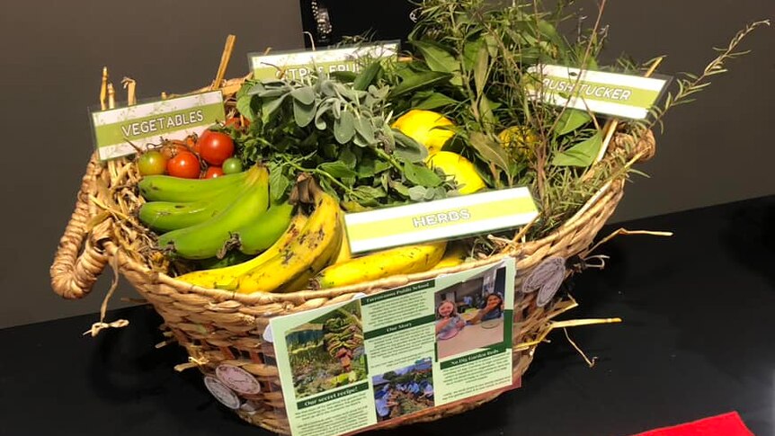 A basket of fruit and vegetables sitting on a table with a red ribbon in front of it.