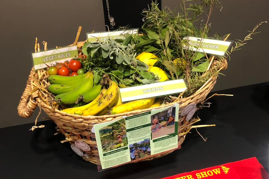 A basket of fruit and vegetables sitting on a table with a red ribbon in front of it.