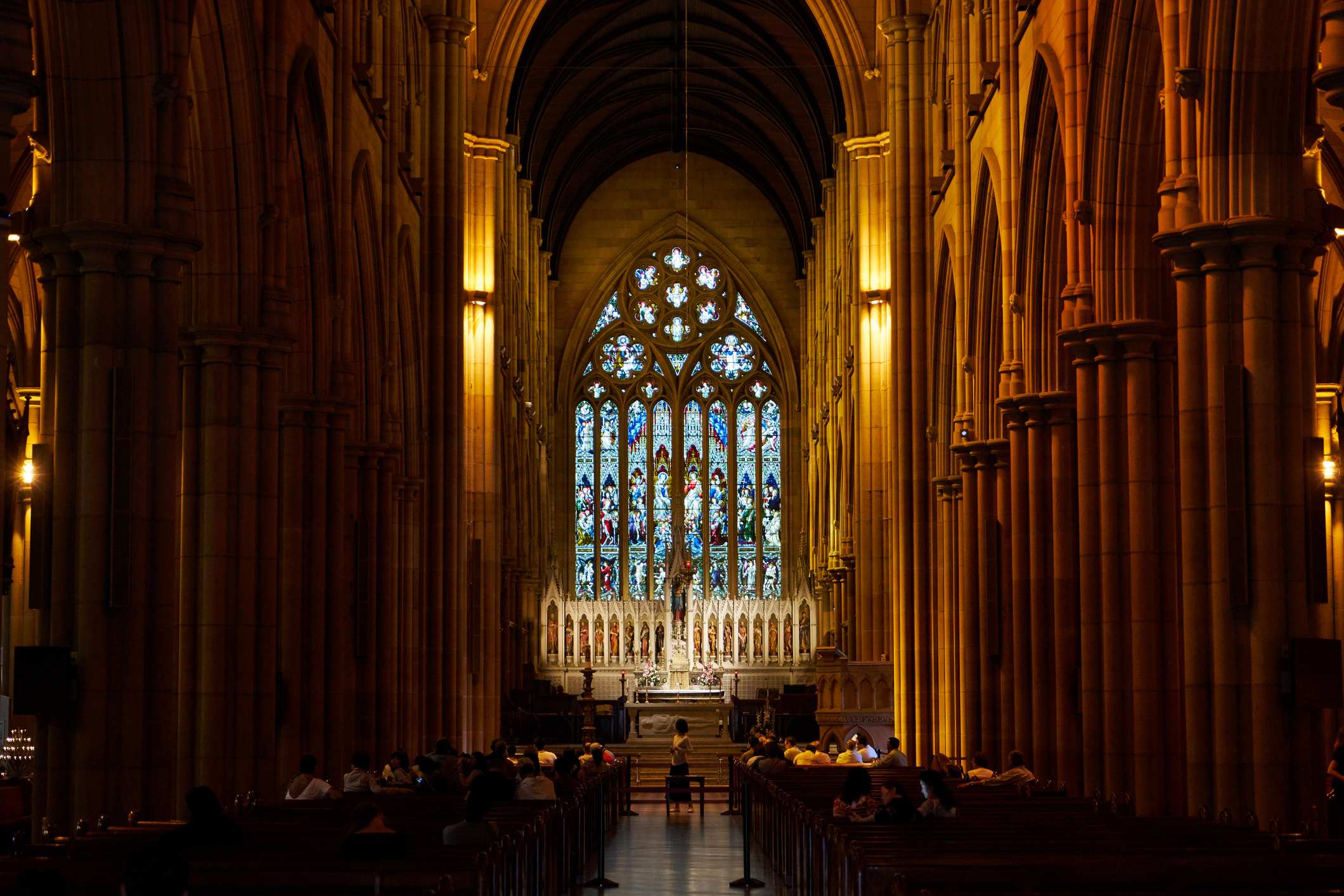 inside of large gothic-style church cathedral with rows of pews facing stained glass window in middle
