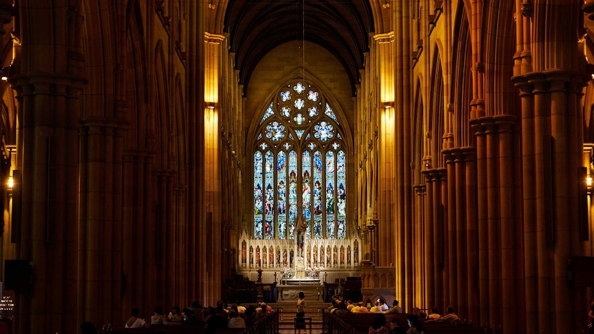 inside of large gothic-style church cathedral with rows of pews facing stained glass window in middle