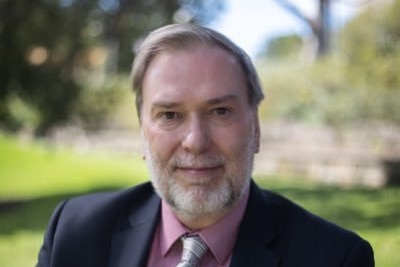 man in suit with silver tie and pink shirt smiles at the camera