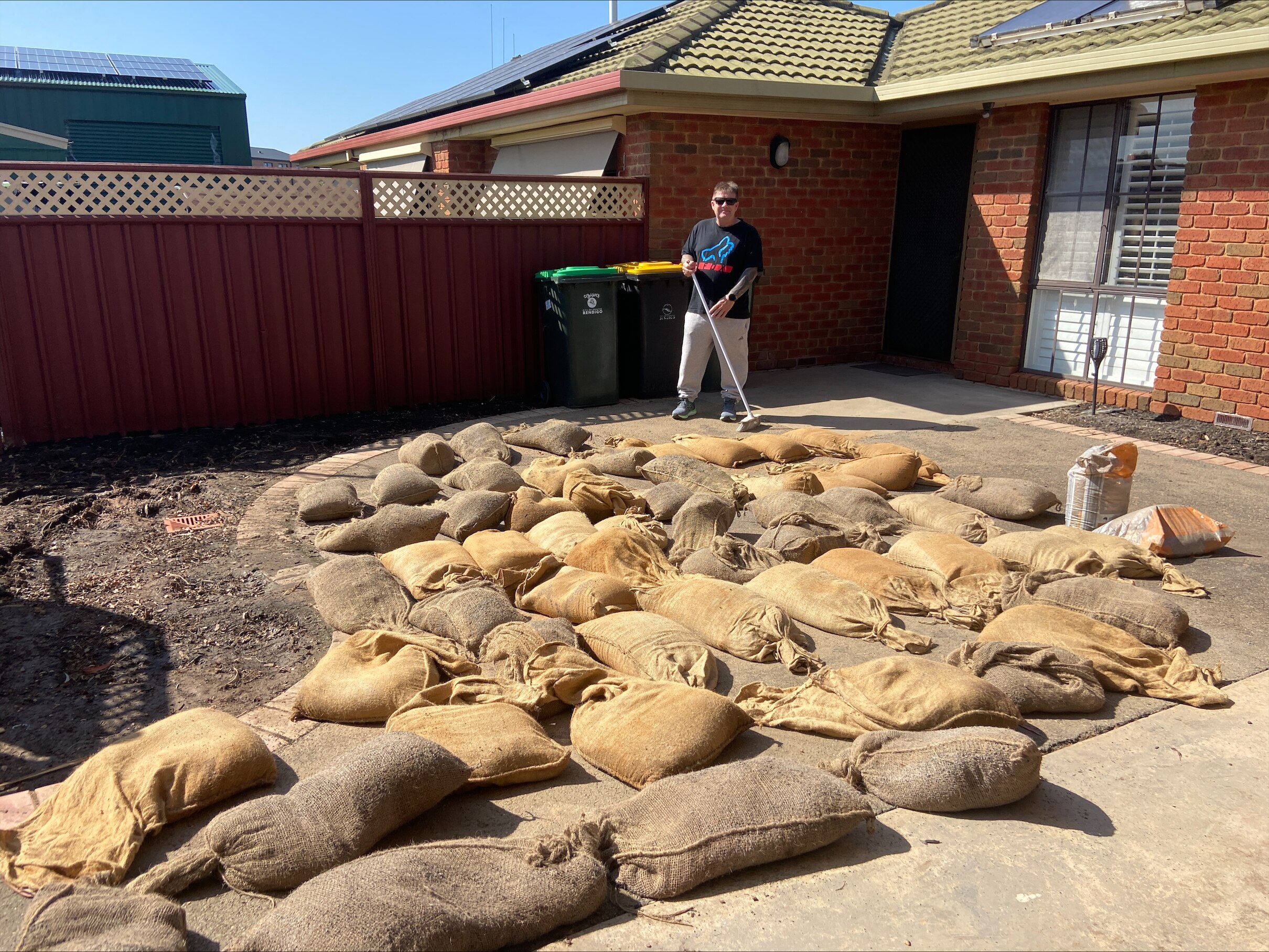 A man cleaning up around the outside of his house, with sandbags on the floor.