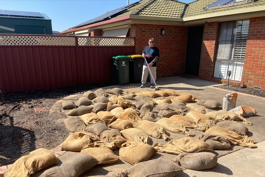 A man cleaning up around the outside of his house, with sandbags on the floor.