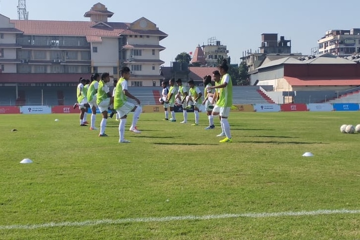 A team of women practices bouncing soccer balls on their knees.