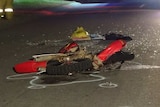 The shattered remains of a dirt bike lie on the road, as emergency services officers stand to one side.