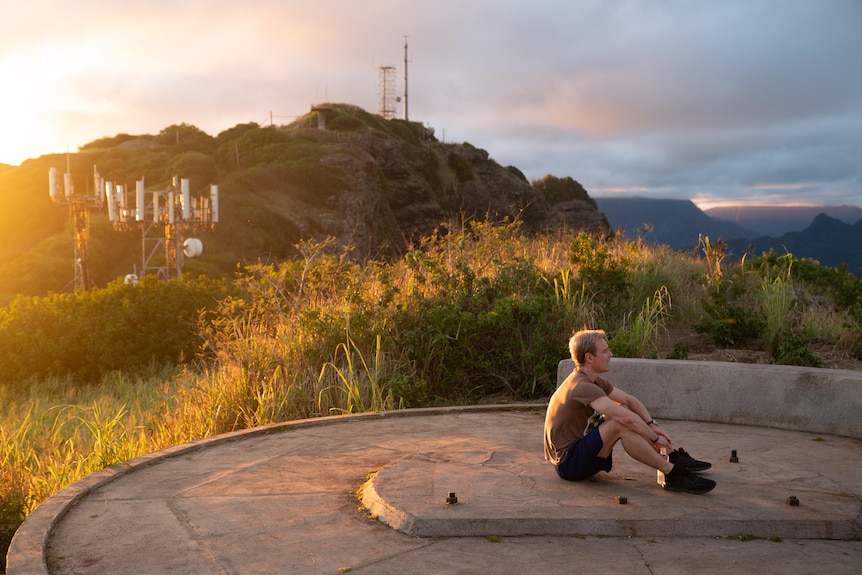 A film still of Michael Fassbender in running clothes, sitting with his arms on his knees on top of a hillside.