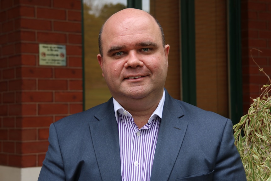 A head and shoulders shot of Bradley Woods who is wearing a suit and standing outside a brick building.