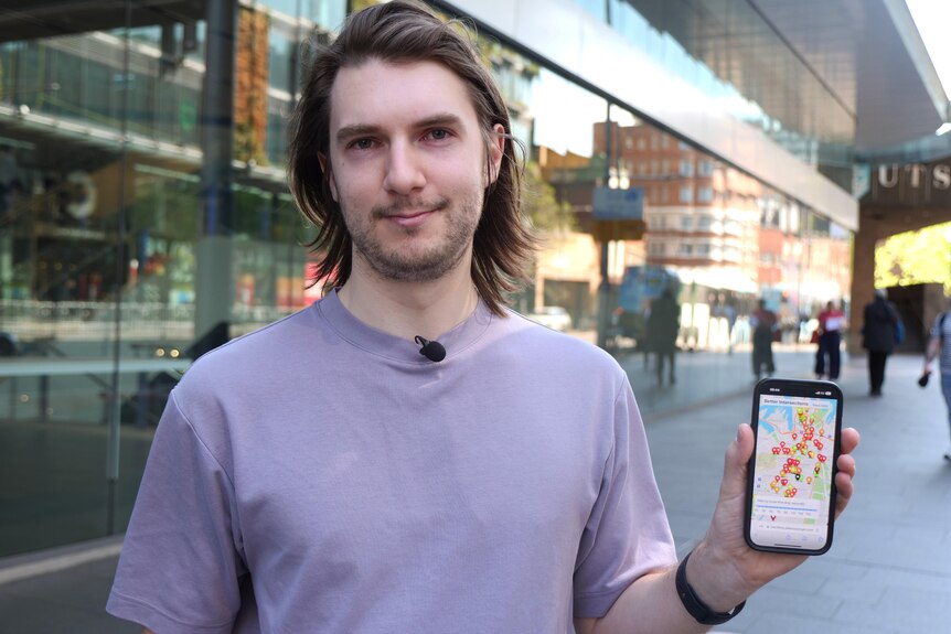 A young man holding a phone showing a map of Sydney