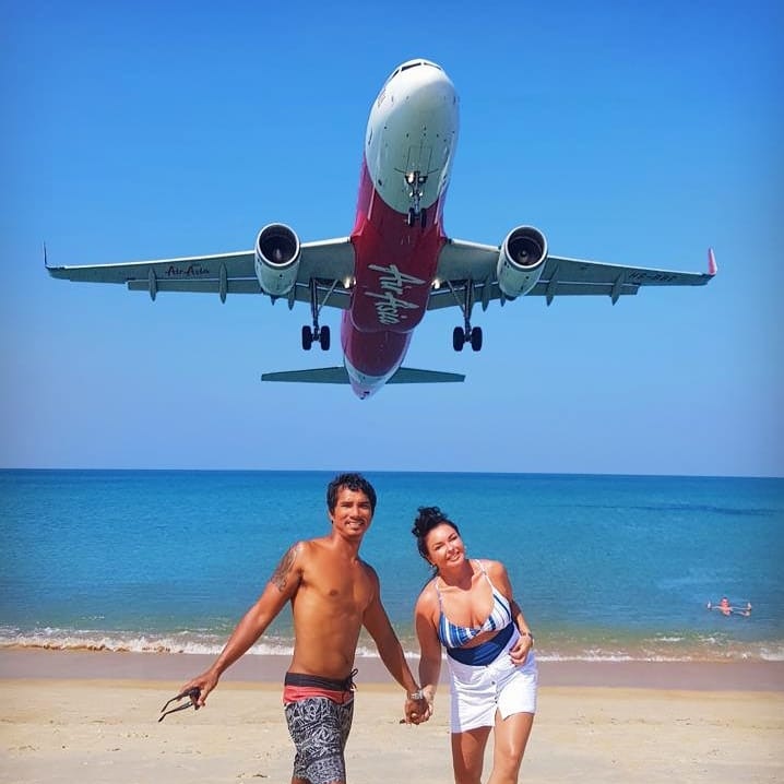 Schapelle Corby and a friend wearing beach gear stand on the sand as a plane flies over head