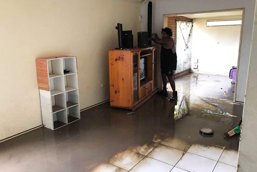 A person stands in the flood-damaged lounge room with muddy water of Donald Mosby's home in Mundingburra.